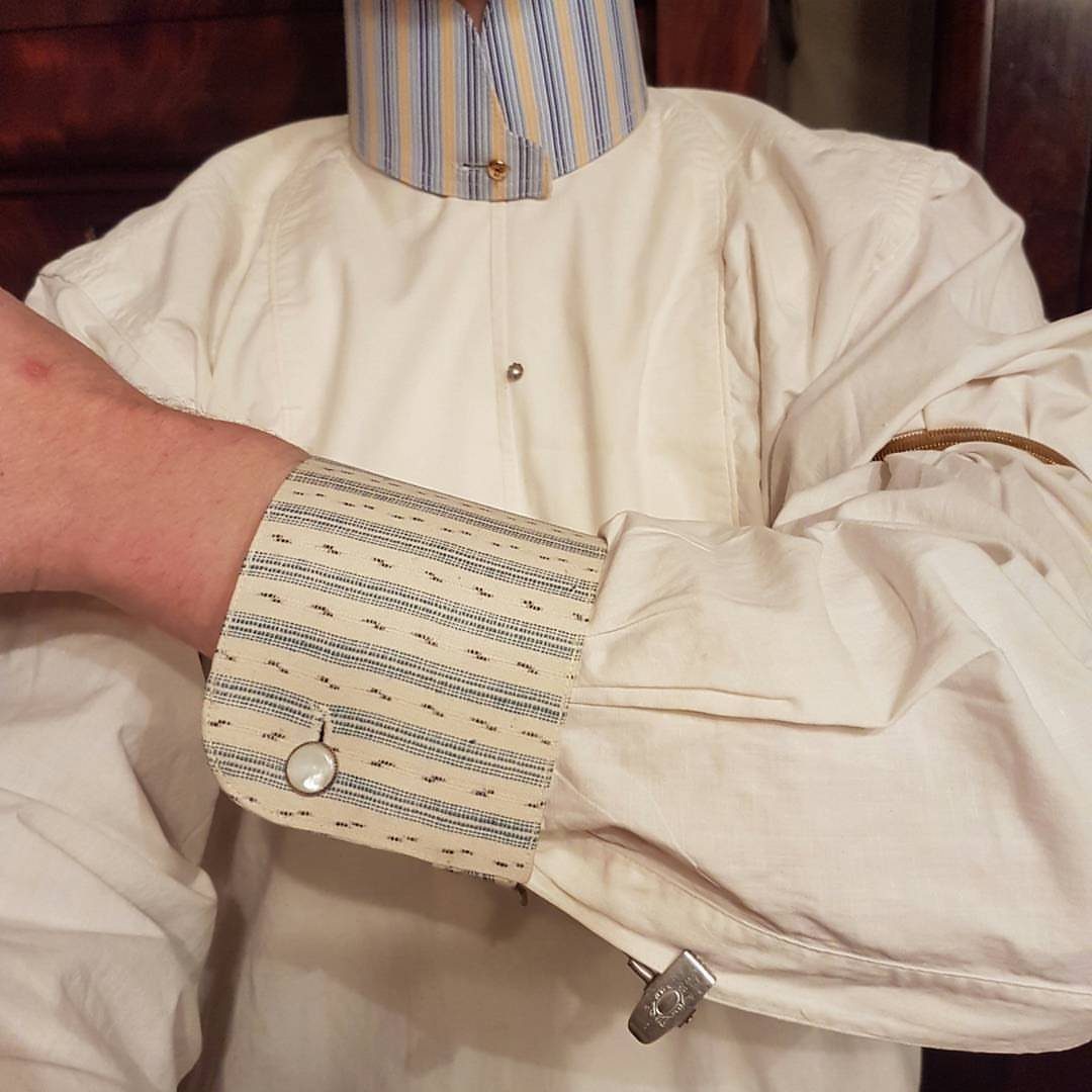 A person wearing a white shirt with striped collar and patterned cuffs.