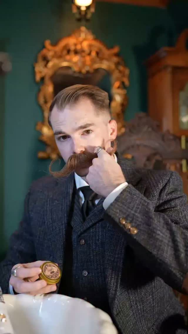 Man with a large handlebar mustache grooming his facial hair with a small comb.