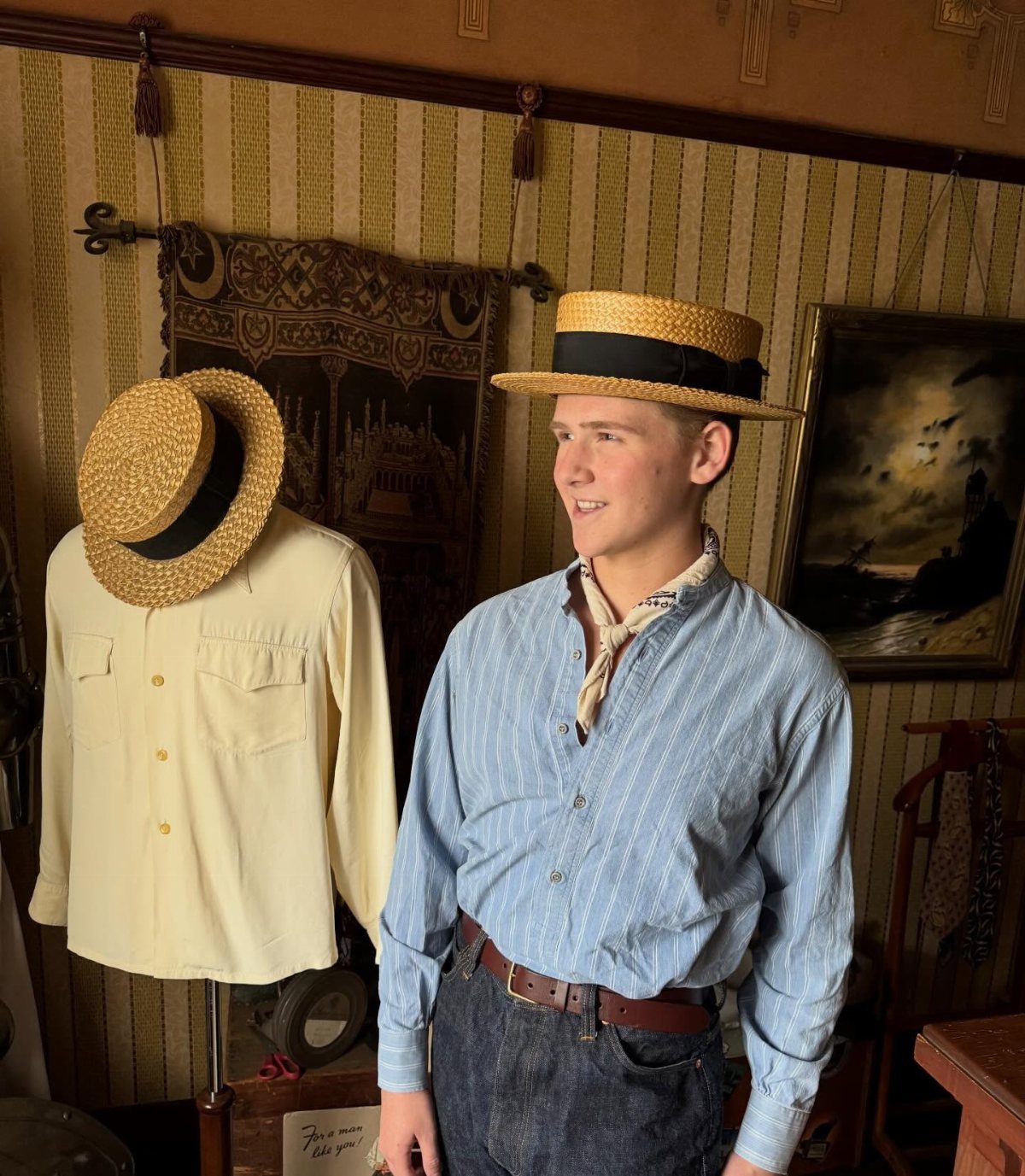 A young man smiling while wearing a vintage straw boater hat and striped shirt.