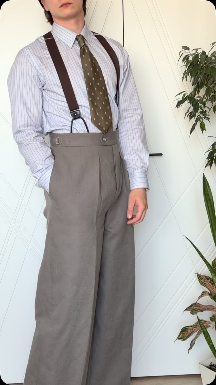 Man wearing wide-leg grey trousers, a striped shirt, patterned tie, and brown suspenders.