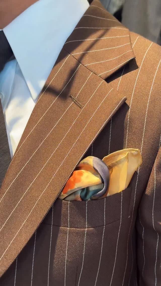 A colorful patterned silk pocket square tucked into the breast pocket of a brown pinstriped suit jacket.