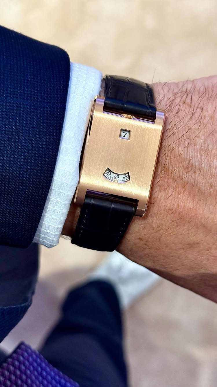 A rectangular gold wristwatch with a black leather strap worn on a man's wrist.