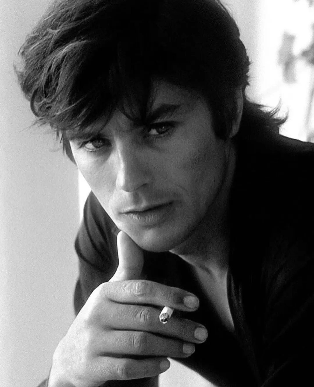 A clean-shaven man with wavy dark hair holding a cigarette in a black and white portrait.