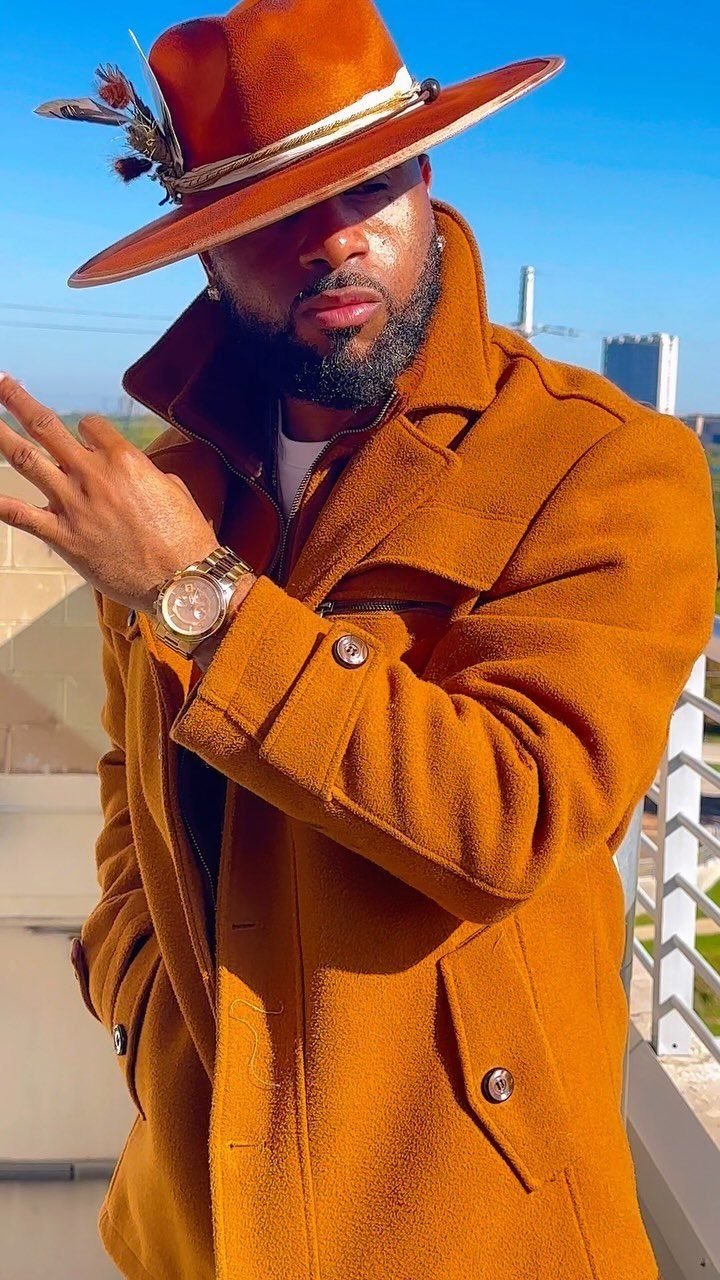 A man wearing an orange fedora hat and a matching orange coat outdoors.
