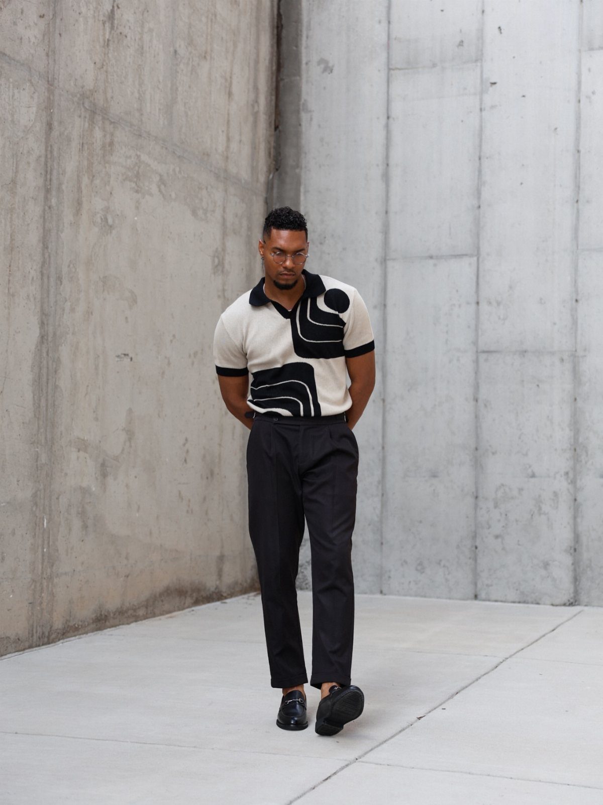 A man wearing a cream polo shirt with bold black geometric patterns and black trousers.