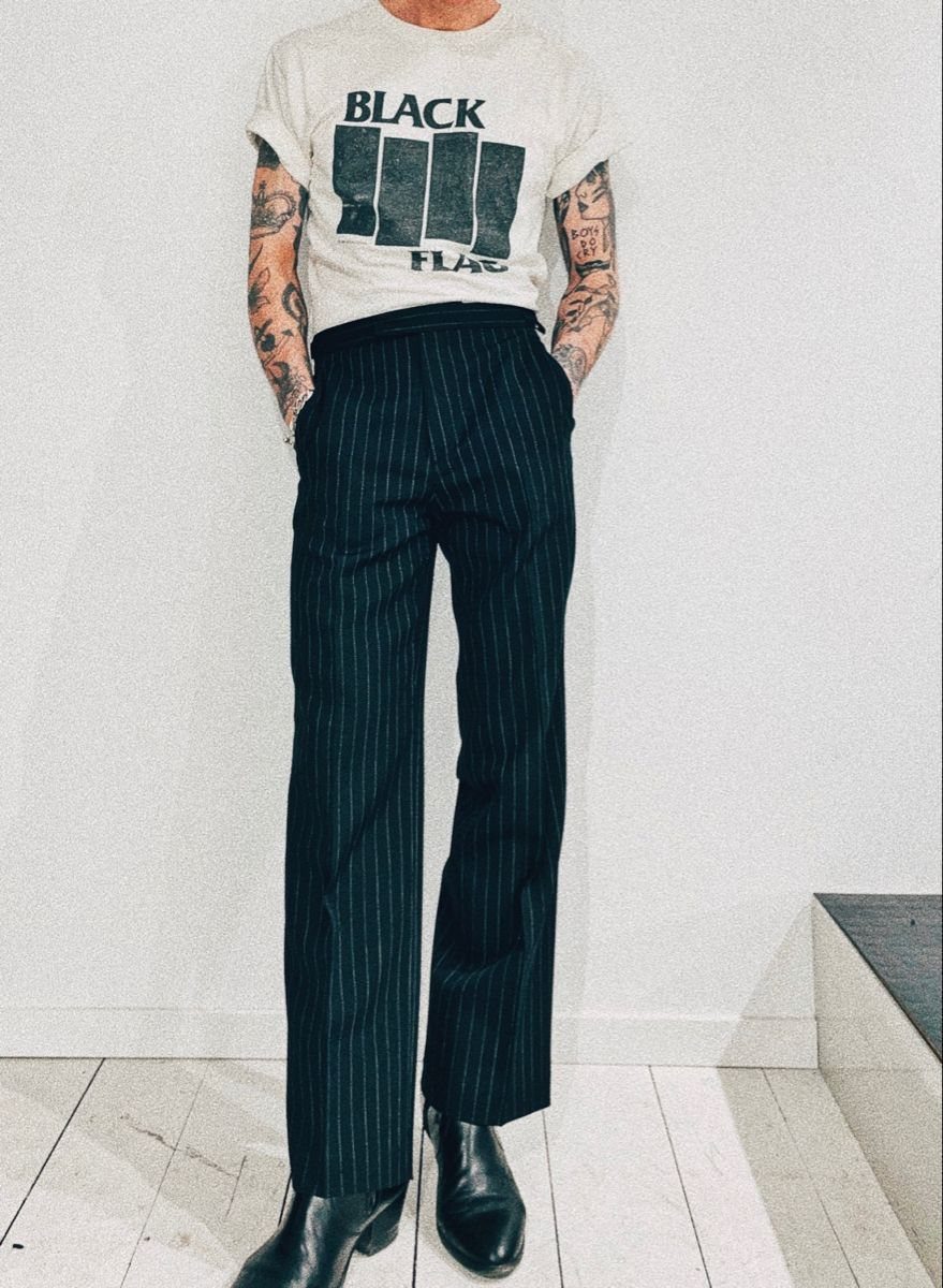 A person wearing a white graphic t-shirt and dark pinstriped slim-fit trousers with black boots.