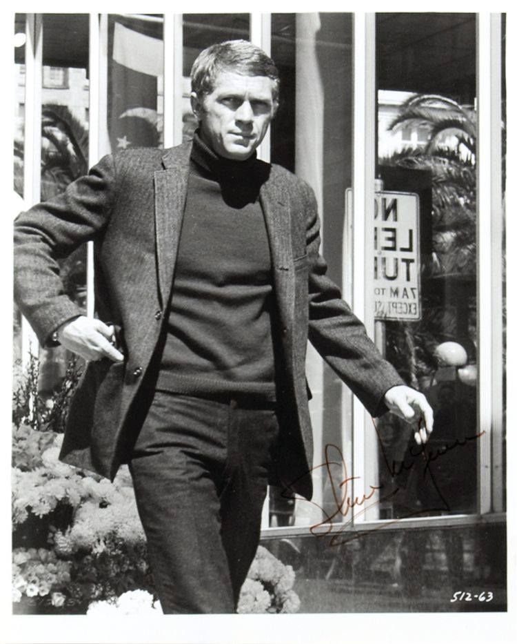 A man wearing a dark turtleneck sweater and blazer walking past a storefront window.
