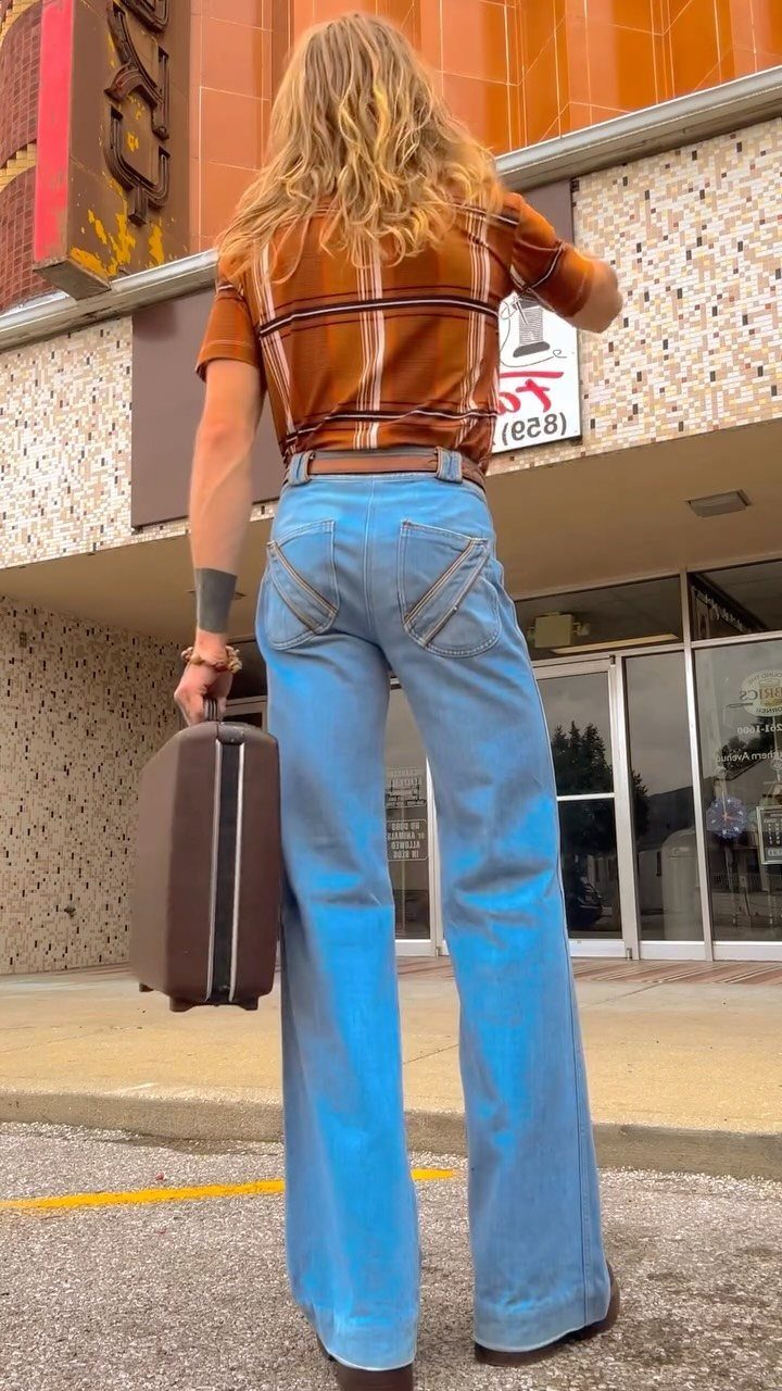 Woman from behind wearing light blue bellbottom jeans and a brown plaid shirt.