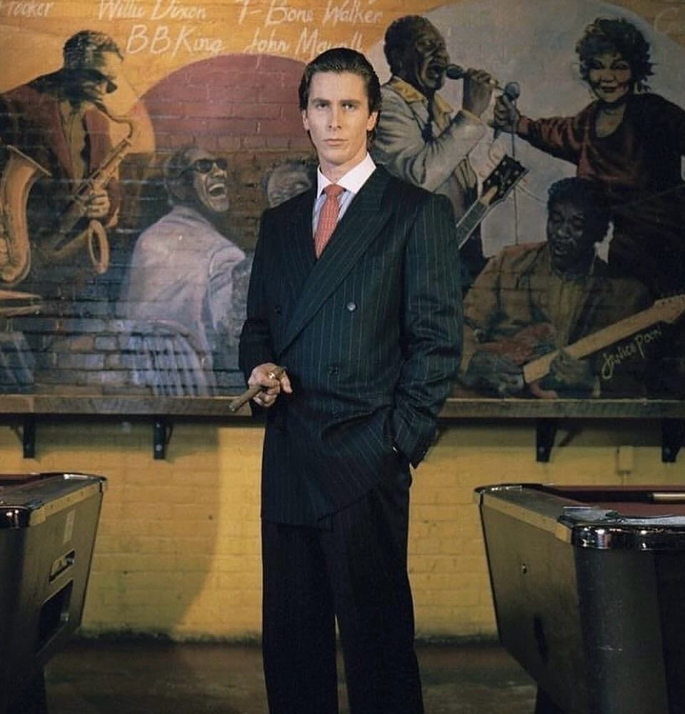 Man in a dark pinstriped double-breasted suit standing in front of a musical mural.