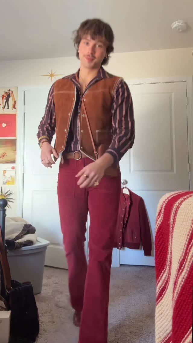 A man wearing a brown vest and red corduroy trousers standing in a room.