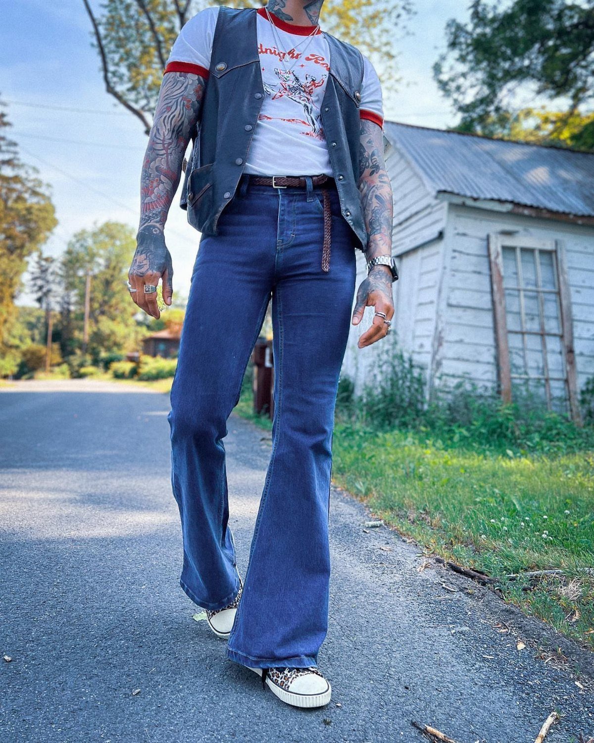 A person wearing blue flared denim jeans and a dark vest standing on a road.