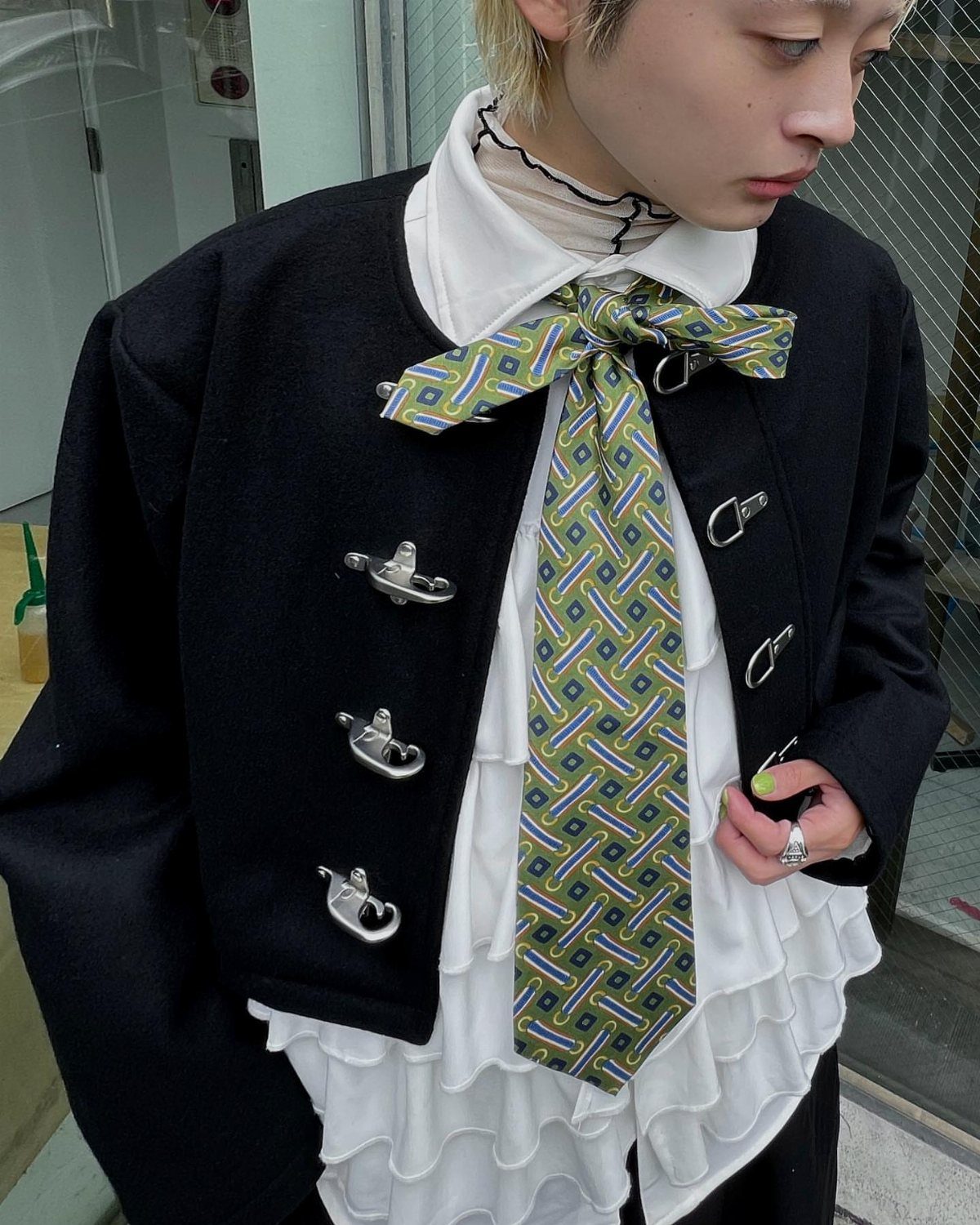 Person wearing a black jacket, white ruffled shirt, and a patterned green necktie tied in a bow.