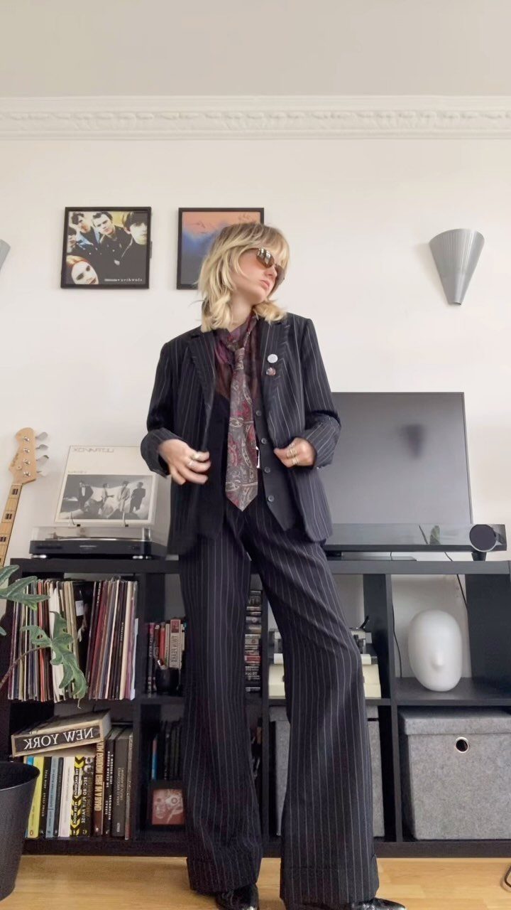 A person posing in a dark pinstripe suit and patterned necktie.