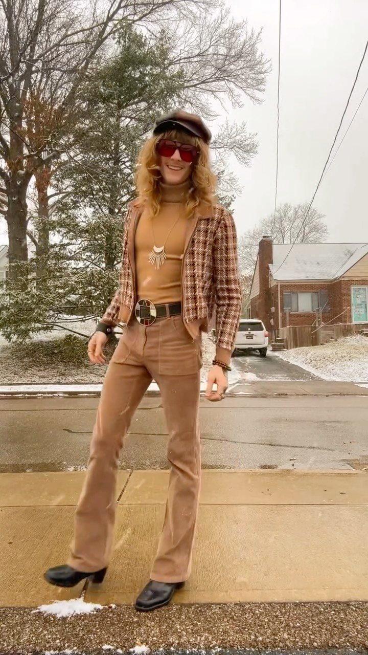 A person dressed in 70s style clothing standing on a snowy sidewalk outdoors.