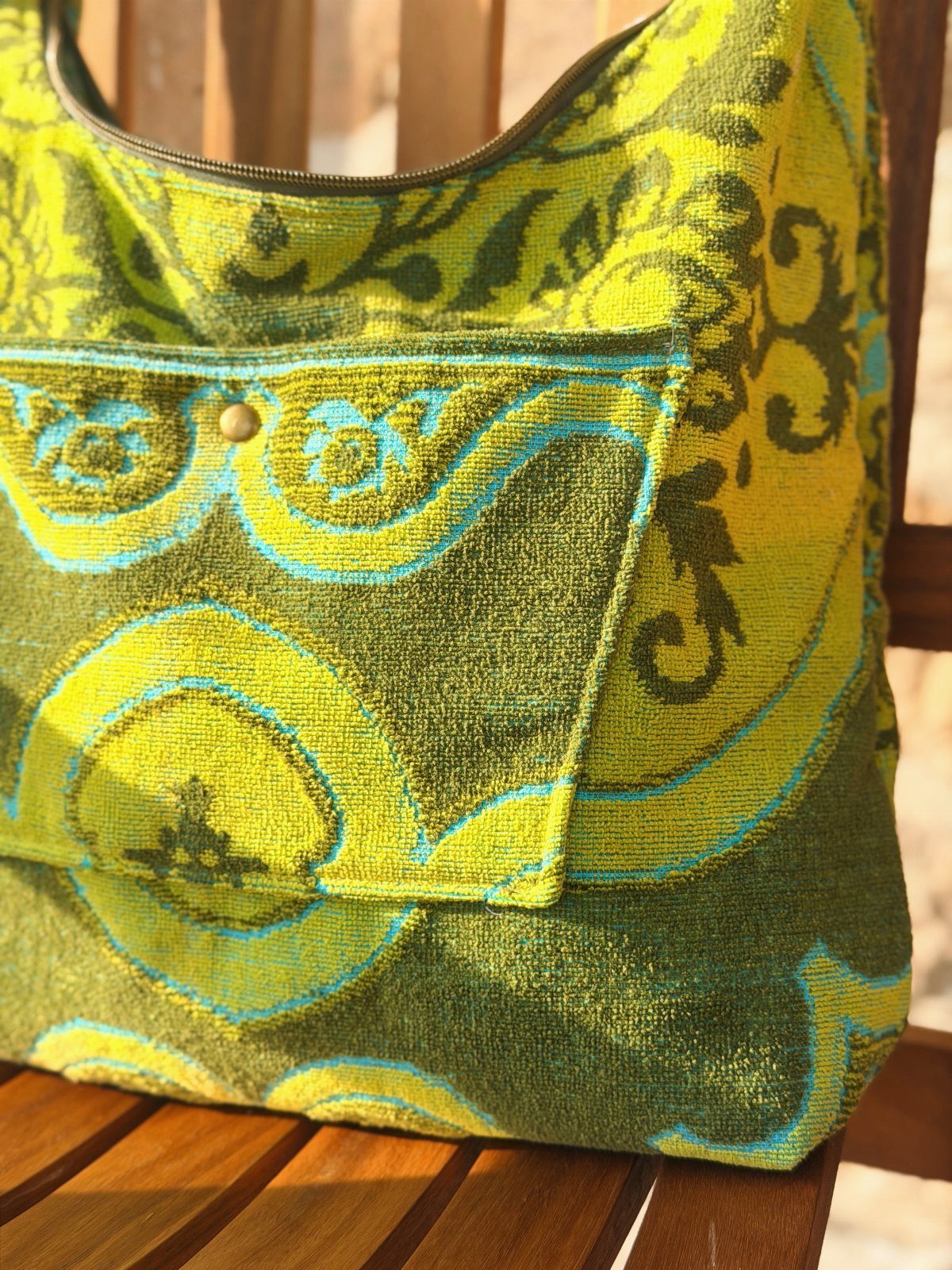 A lime green and olive patterned tapestry handbag resting on a wooden slatted chair.