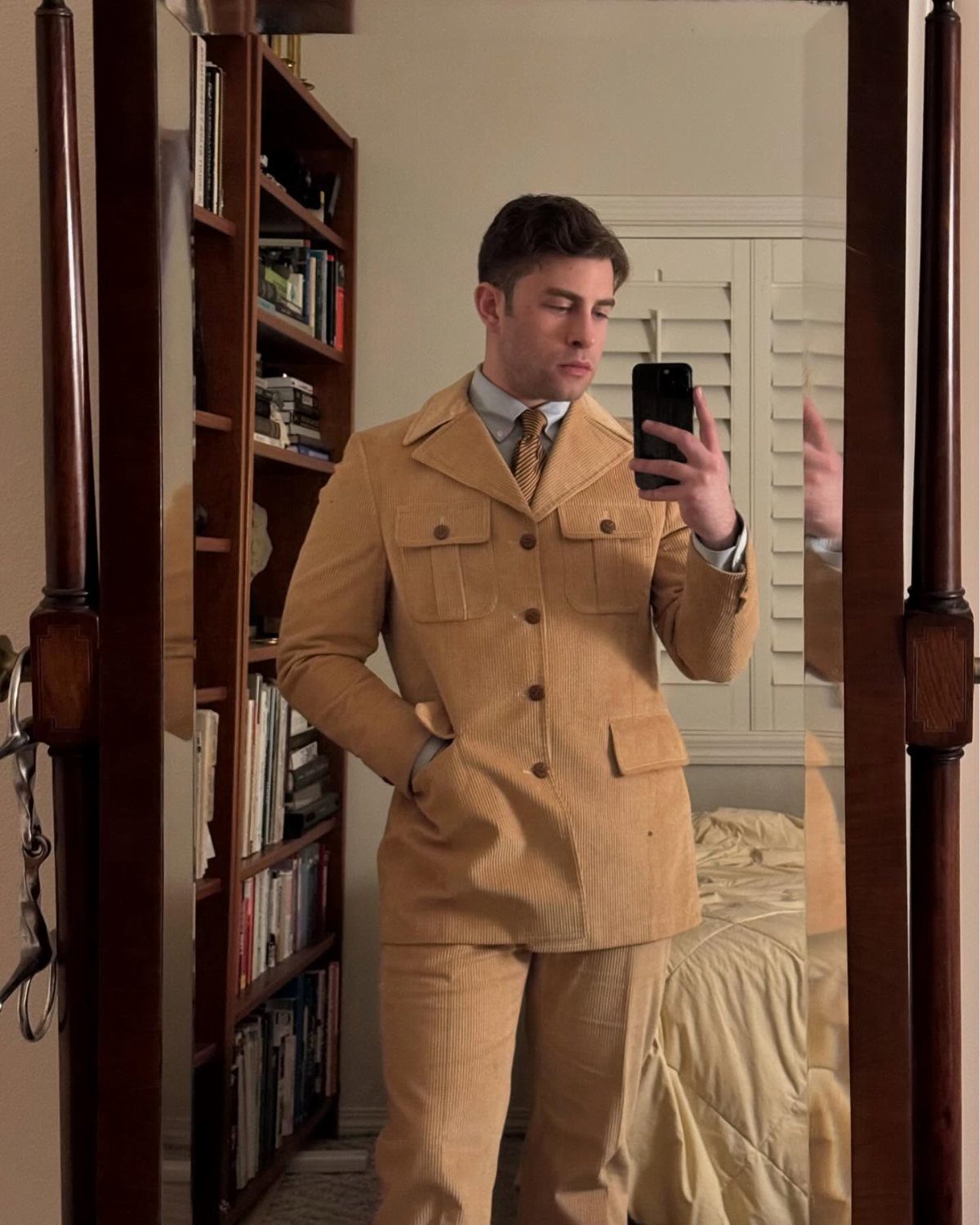 A man posing in a mirror wearing a tan corduroy casual suit and patterned tie.