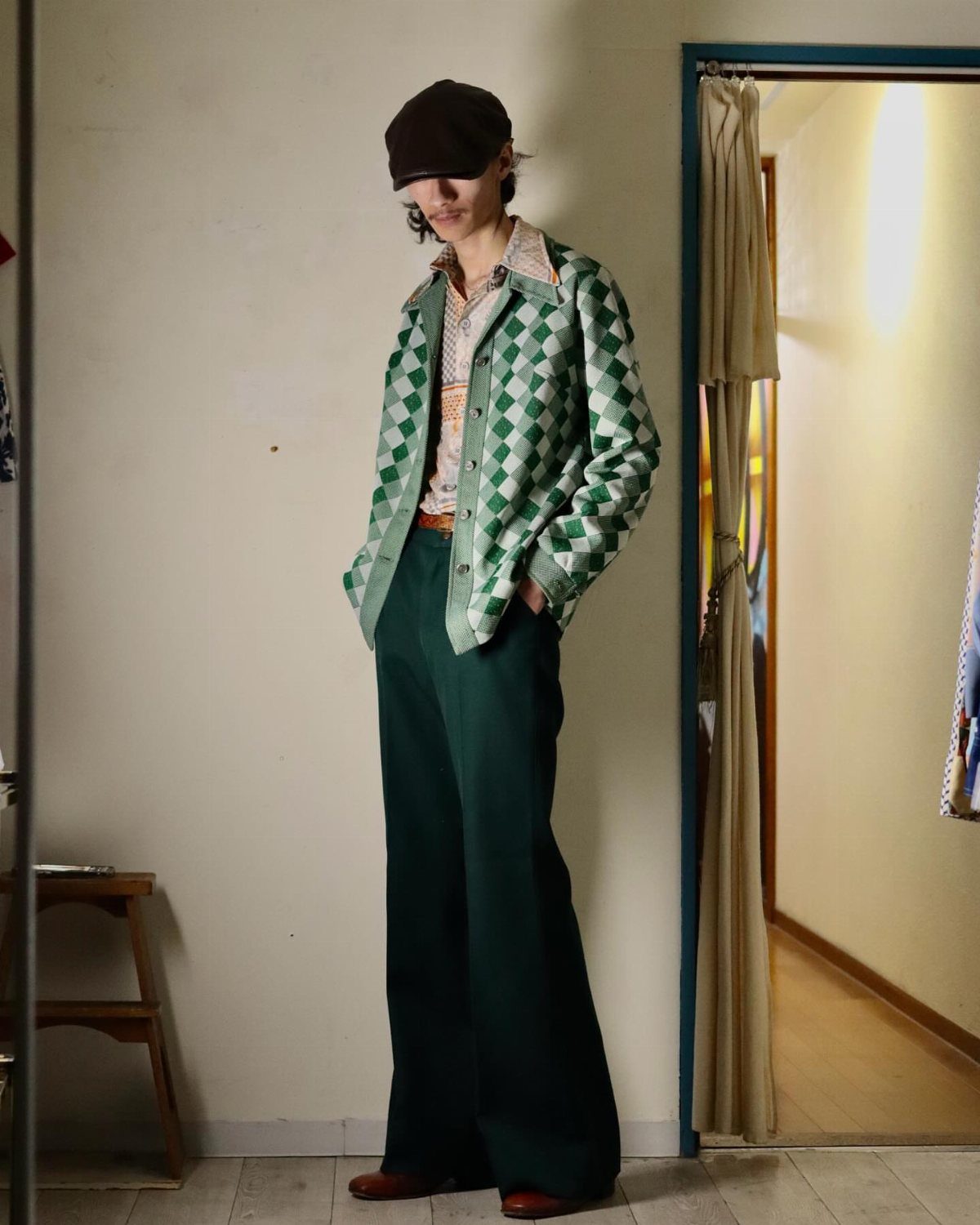A person standing in a room wearing a green geometric patterned jacket and dark green trousers.
