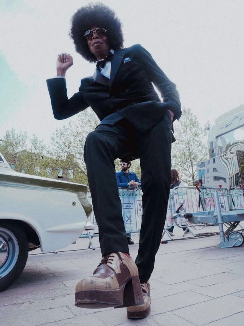 A man with an afro wearing a black suit and large brown platform shoes.
