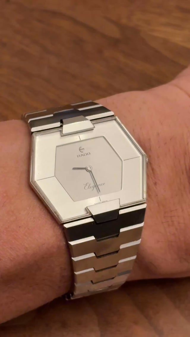 A silver octagonal metal watch with a linked bracelet worn on a person's wrist.