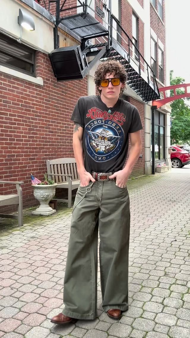 A young man posing in a vintage graphic t-shirt and wide-leg olive trousers.