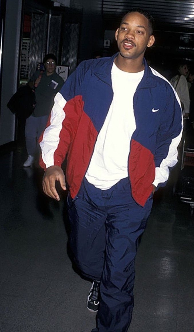 Man walking in a colorful navy, red, and white Nike windbreaker and navy trousers.