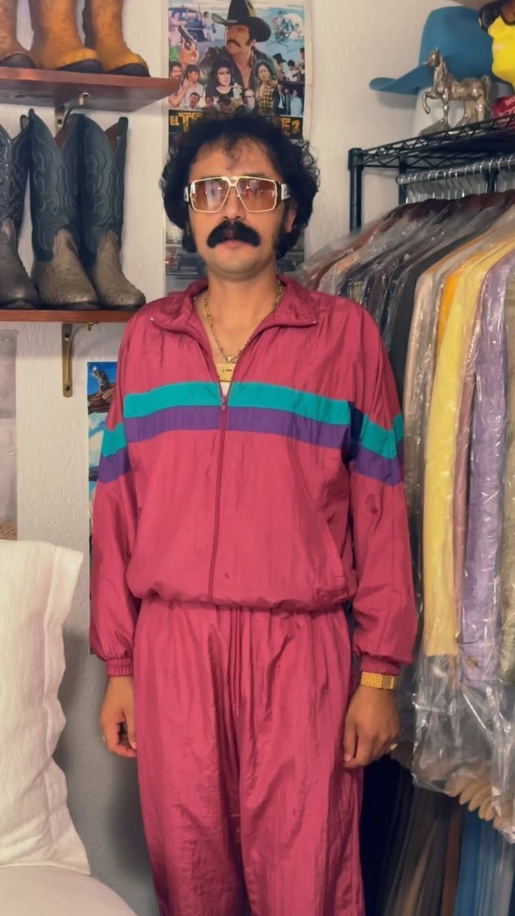 A man wearing a magenta and teal color-blocked tracksuit and large glasses.