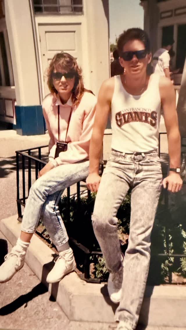 A man and woman posing in light-colored acid-wash denim jeans and sunglasses.