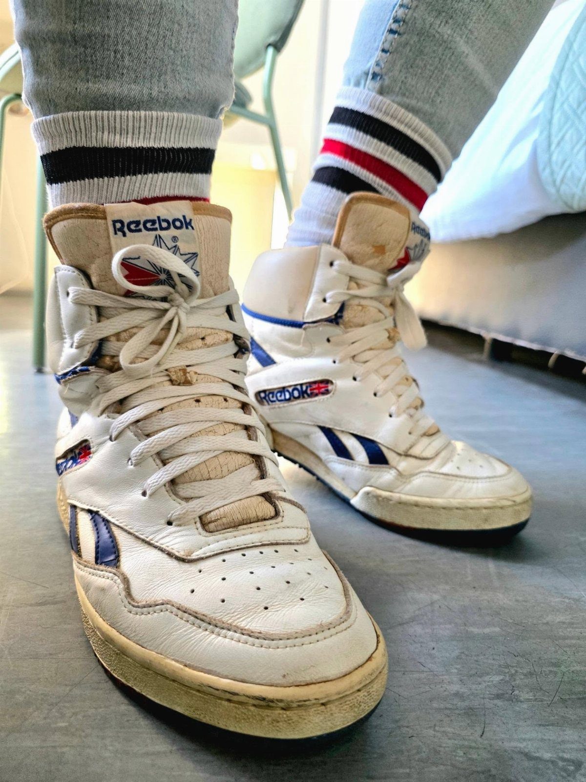 White high-top Reebok sneakers with blue accents worn with striped socks and light blue jeans.