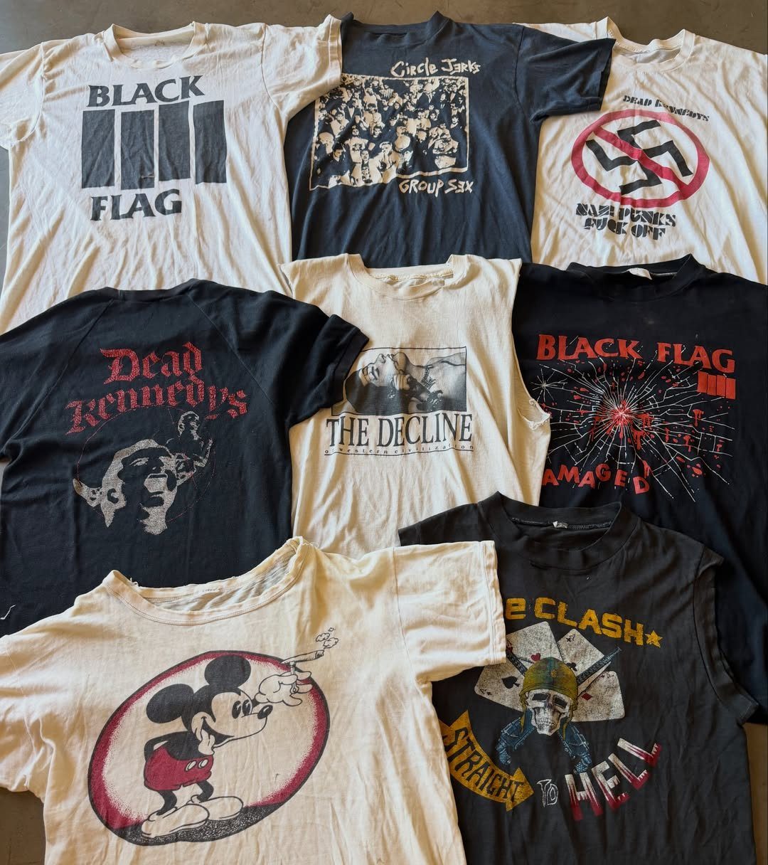 Vintage graphic t-shirts with various band logos and punk rock designs spread across a surface.