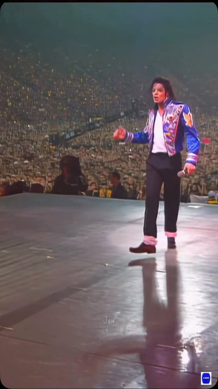 Michael Jackson performing on a stage in a blue embroidered jacket and black pants.