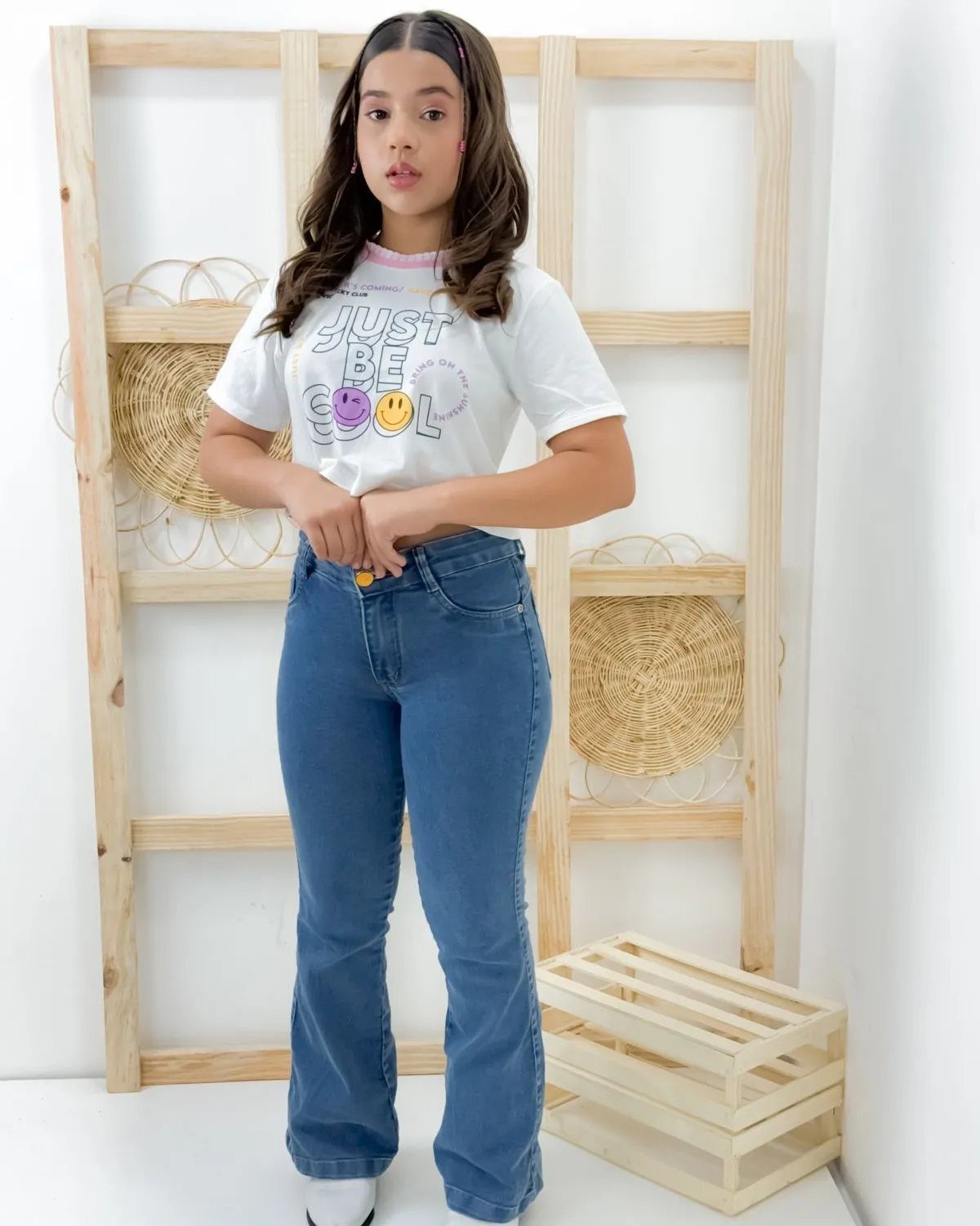 A young girl wearing a white graphic t-shirt and blue high-waisted flared jeans.