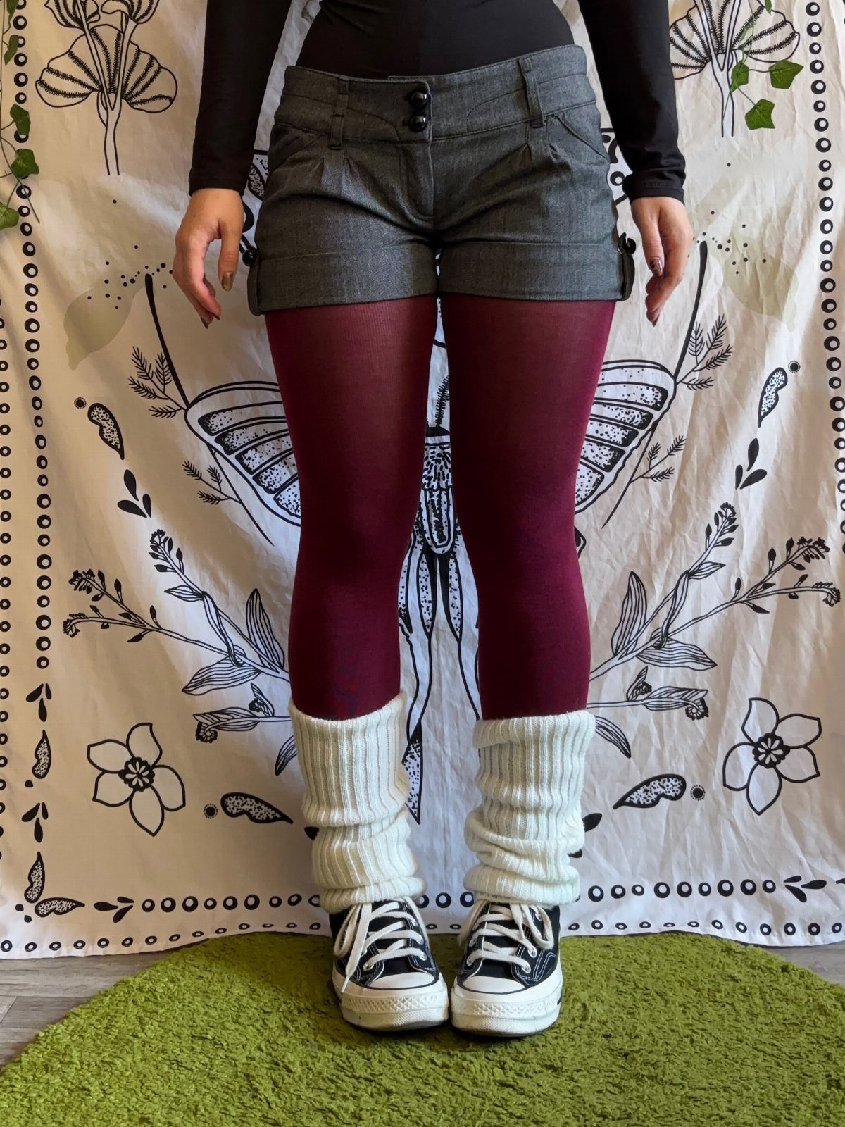 Person wearing burgundy leggings with white ribbed leg warmers and black sneakers.
