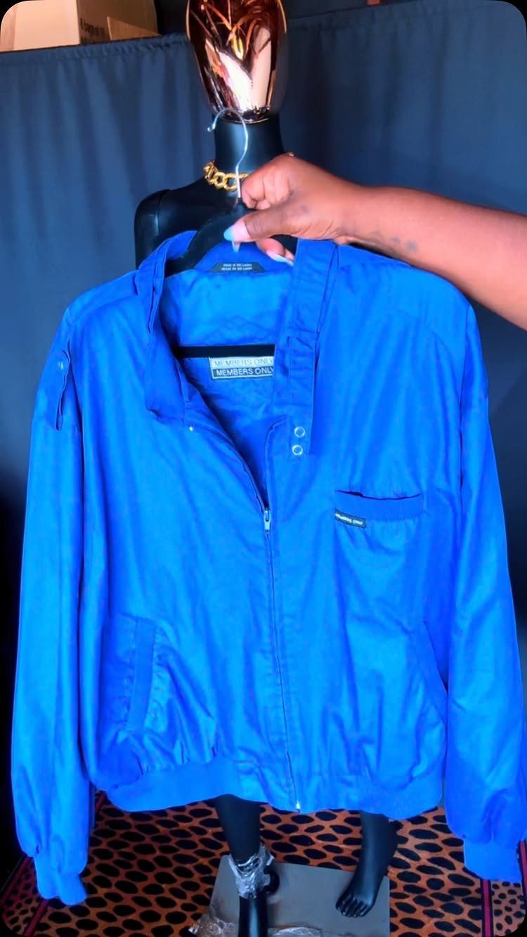 Bright blue Members Only style jacket hanging on a black mannequin against a dark background.