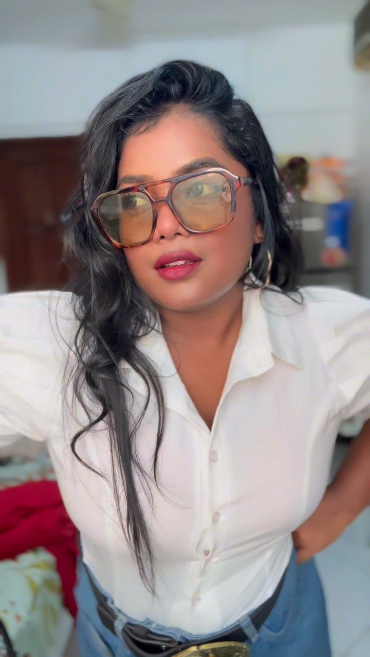 Woman wearing a white shirt with large puffed sleeves and oversized tinted glasses.