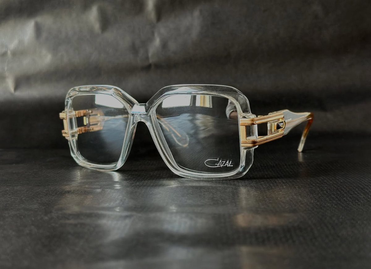 Clear oversized Cazal glasses with gold metal accents resting on a dark textured surface.