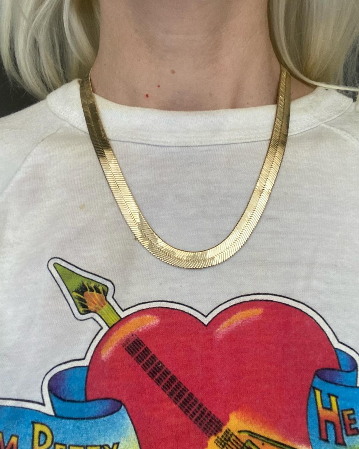 A thick gold curb chain necklace worn over a white graphic t-shirt.