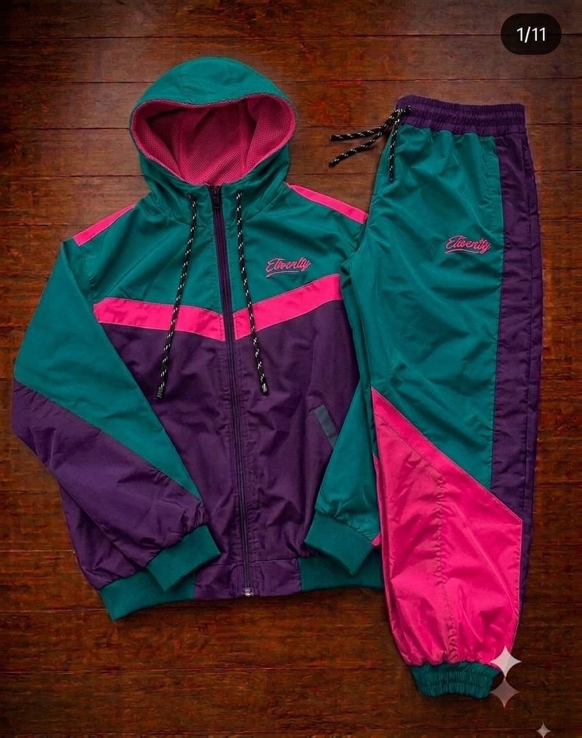 A teal, pink, and purple color-blocked hooded tracksuit laid flat on a wooden background.