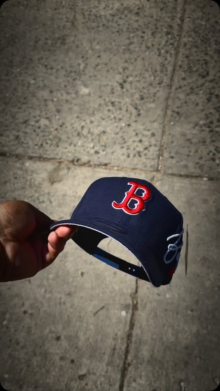 A hand holding a navy blue baseball cap with a red embroidered B logo.