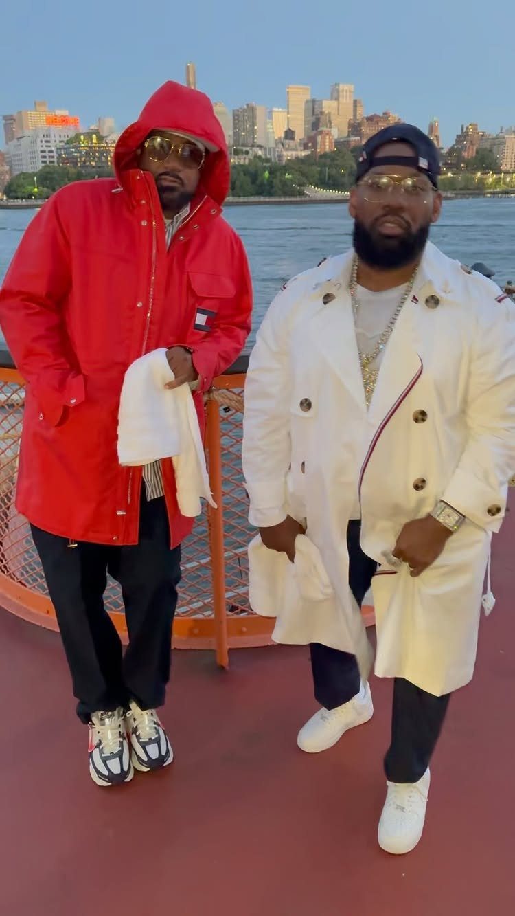 Two men posing in stylish streetwear with a city skyline and water in the background.