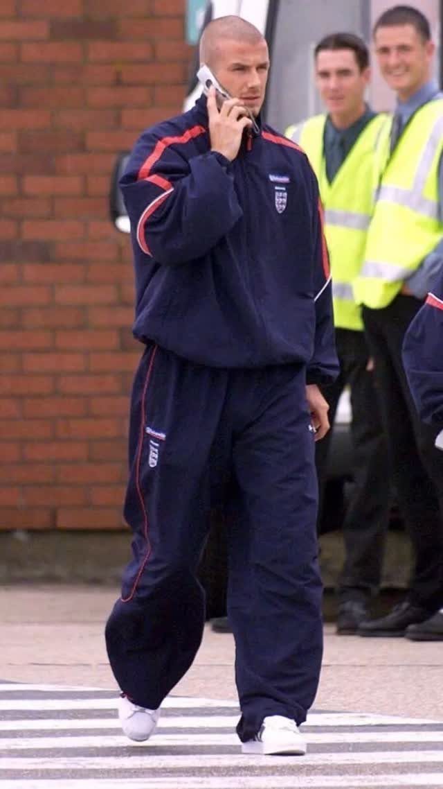 Man in a navy blue tracksuit with red stripes walking while talking on a phone.