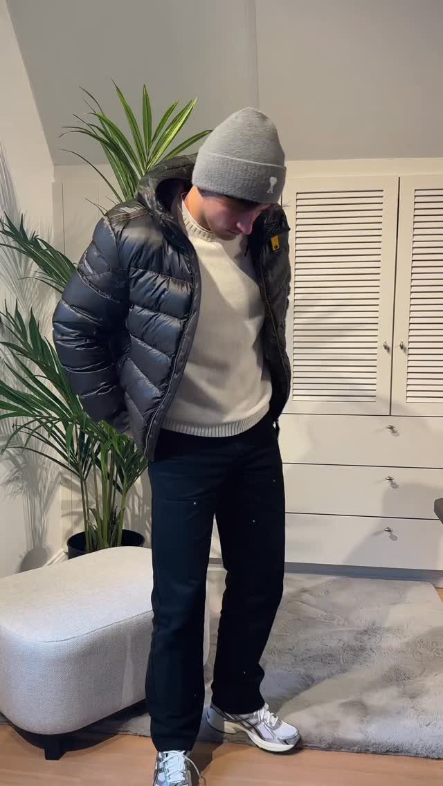 Man wearing a black puffer jacket, white sweater, black pants, and silver Asics Gel sneakers.