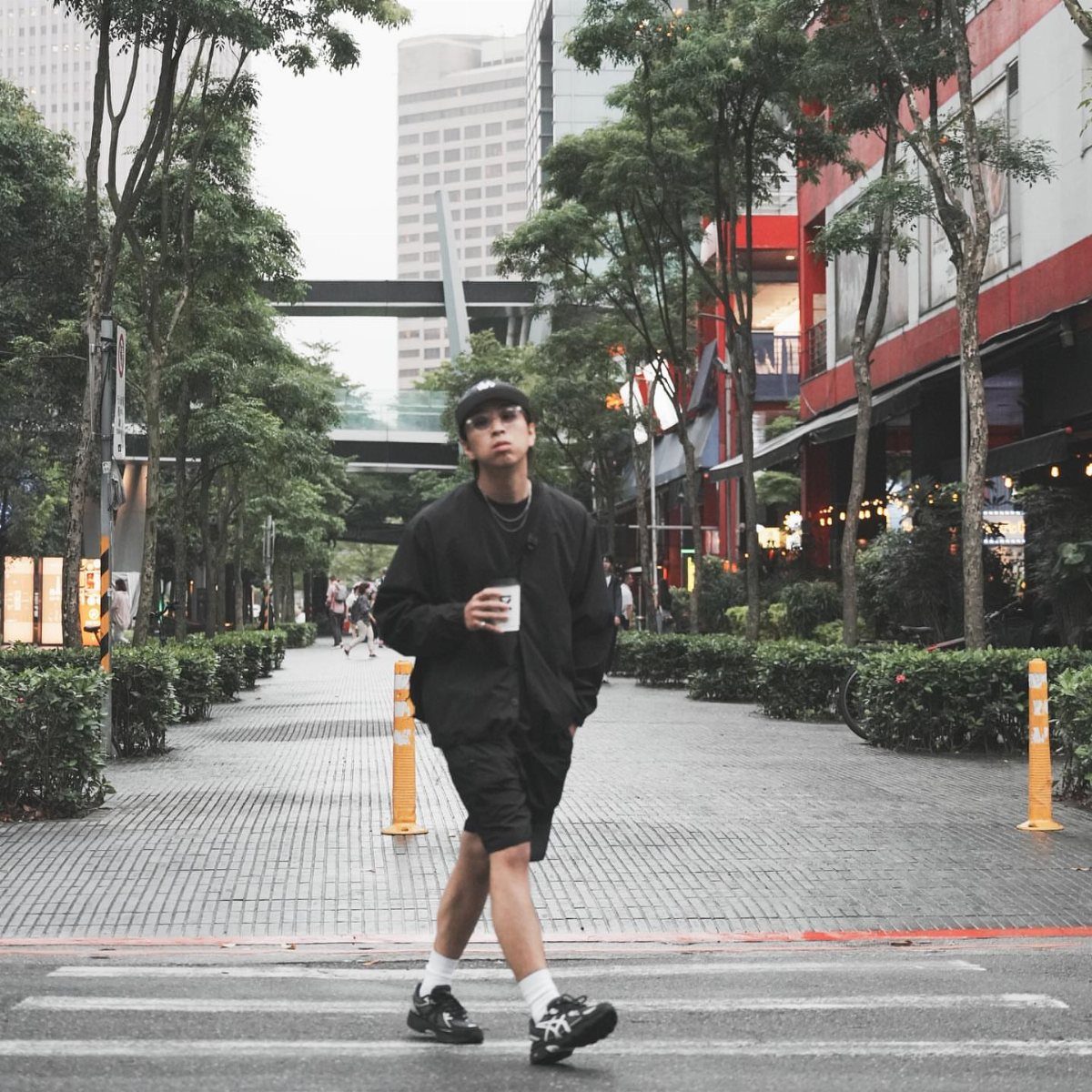A man in a black outfit and Asics sneakers walking through a city street.