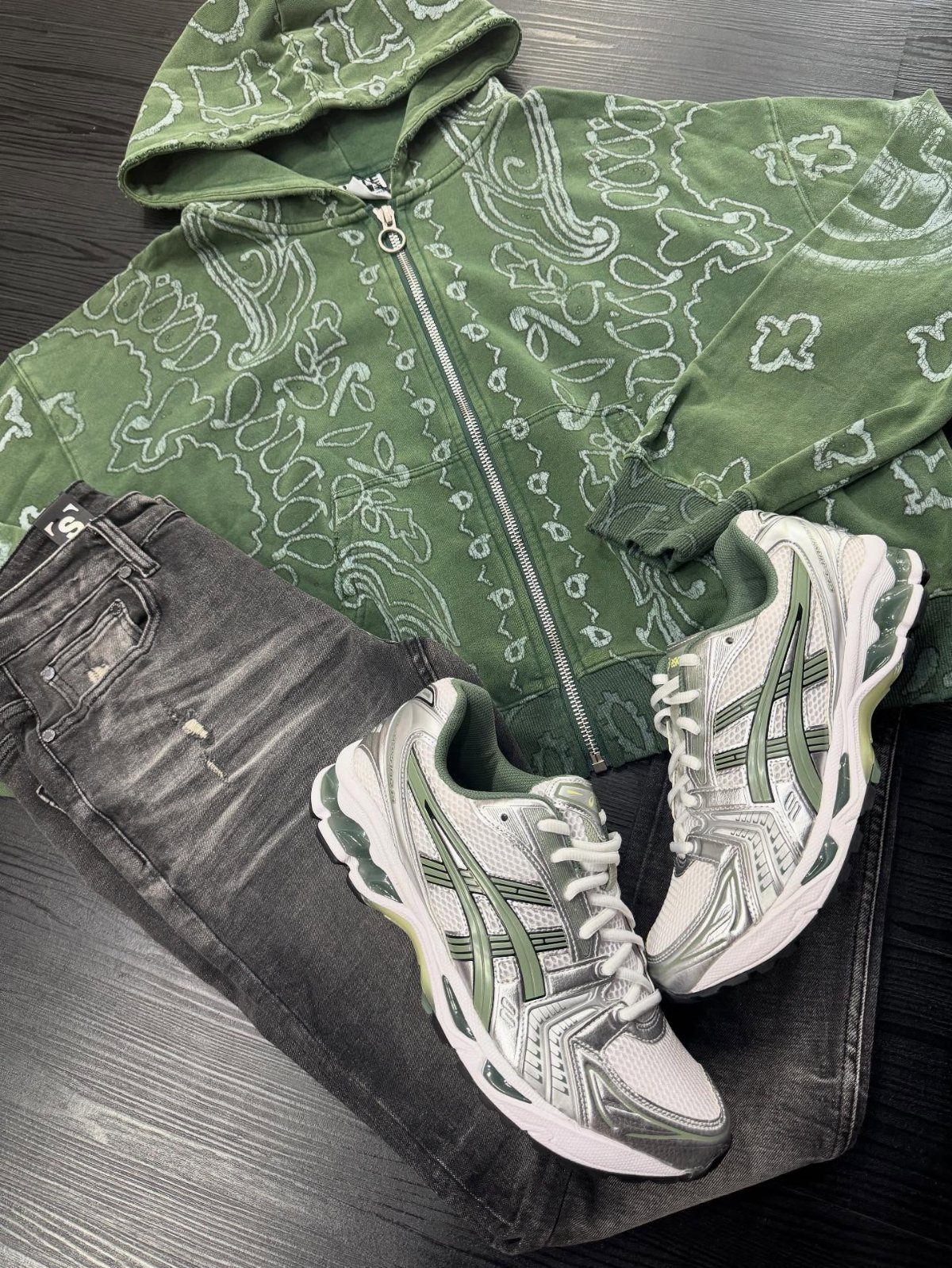 Green patterned hoodie, dark grey jeans, and Asics Gel sneakers laid out on a dark wood surface.
