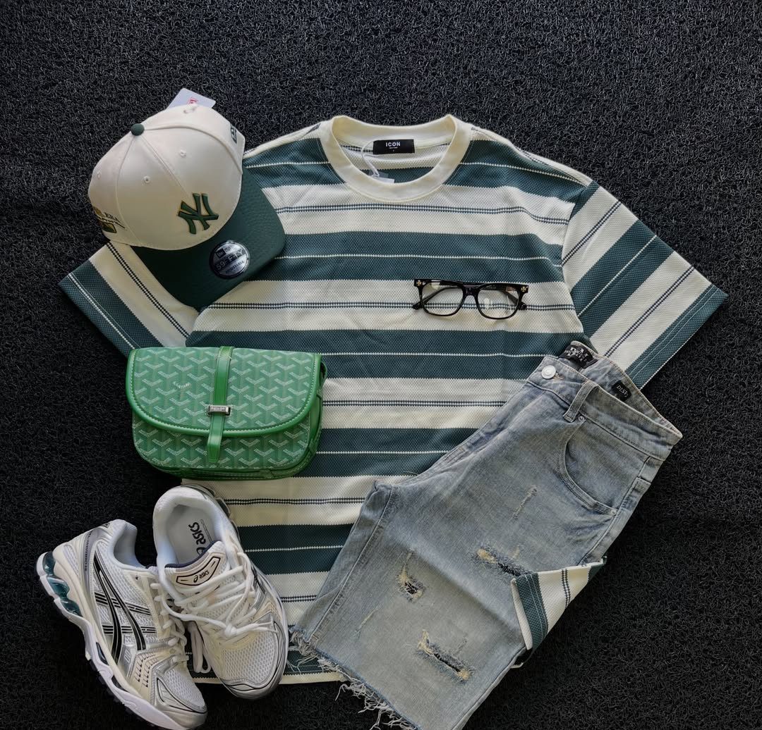 Striped sage green t-shirt, denim shorts, white sneakers, and a green bag laid out on a dark surface.