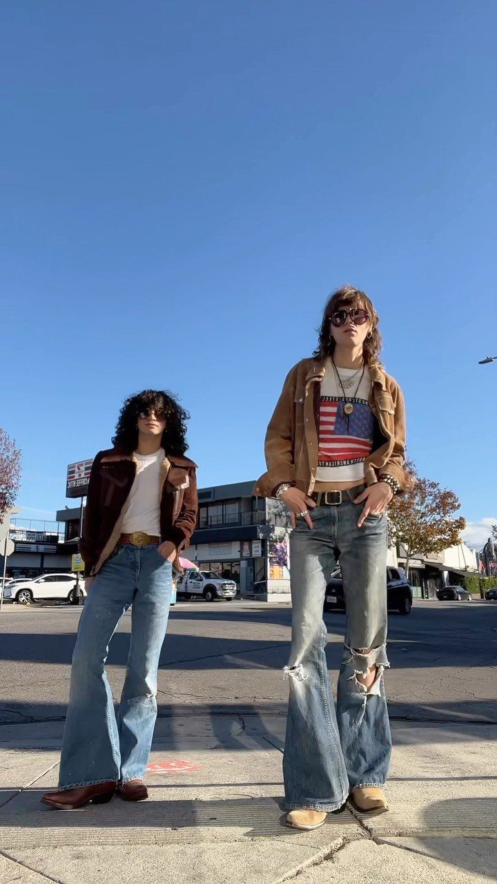 Two men in retro flared jeans and vintage jackets posing on a city street.