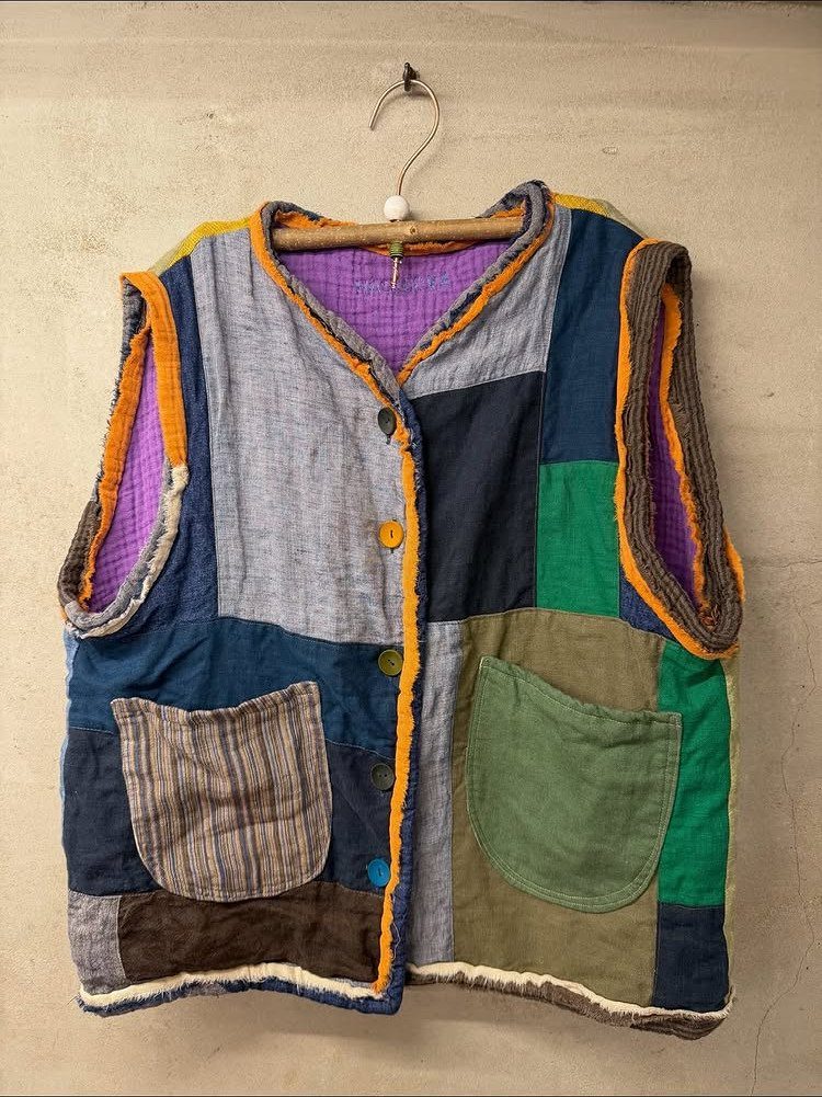 A colorful patchwork vest made of various fabric scraps hanging on a wooden hanger.