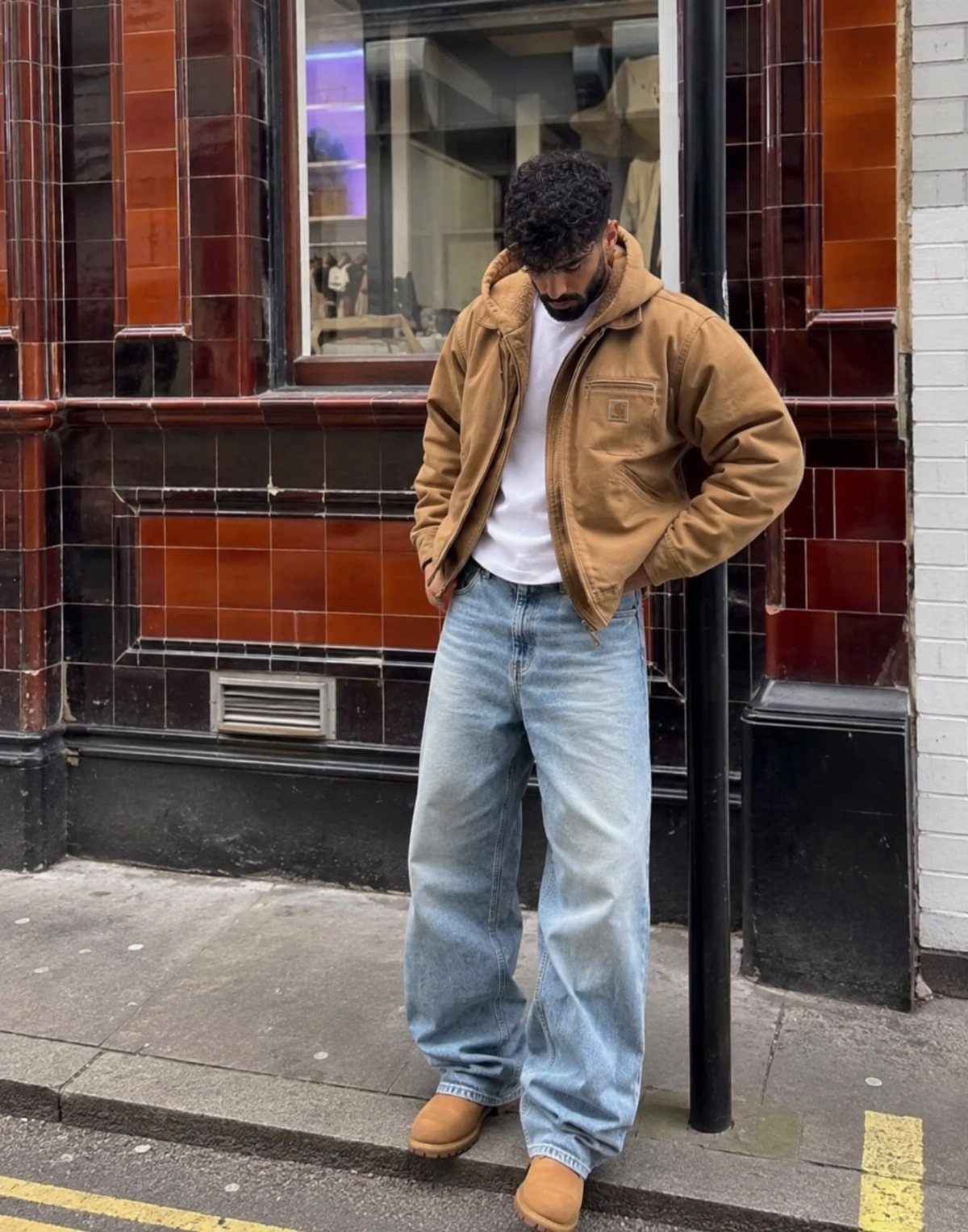 Man wearing a tan work jacket, white t-shirt, and baggy light blue denim jeans.