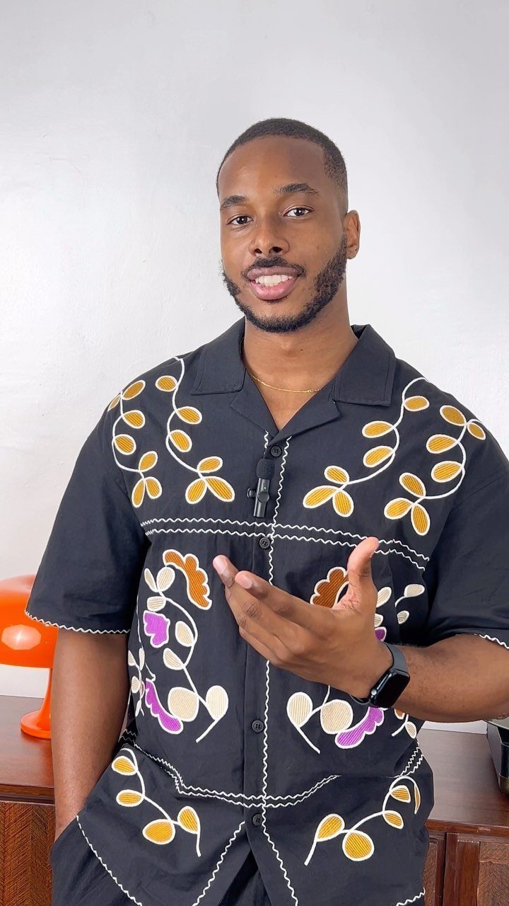 A man wearing a black shirt with vibrant yellow and white floral embroidery patterns.
