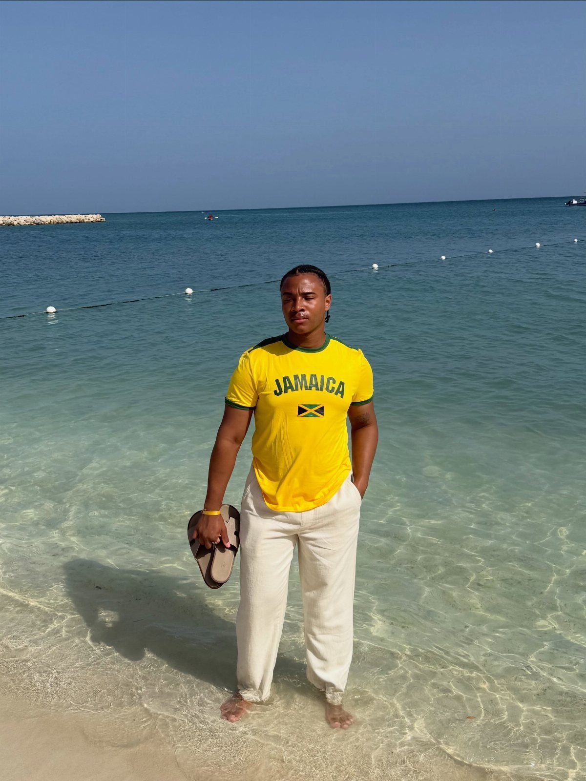 Man in a yellow Jamaica t-shirt and white trousers standing in clear turquoise ocean water.