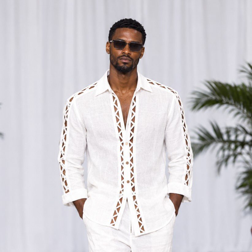 Man wearing a white linen shirt with geometric cutouts and white trousers.